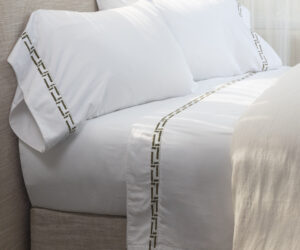 White pillows with a gold geometric border on a beige sofabed edge close up