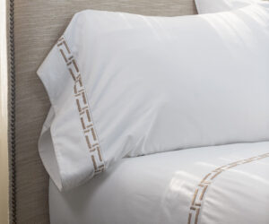Close up of white pillows on a beige upholstered headboard with nailhead trim