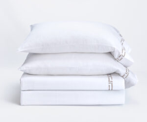 Stack of three white pillows neatly stacked on a pale surface against a white background