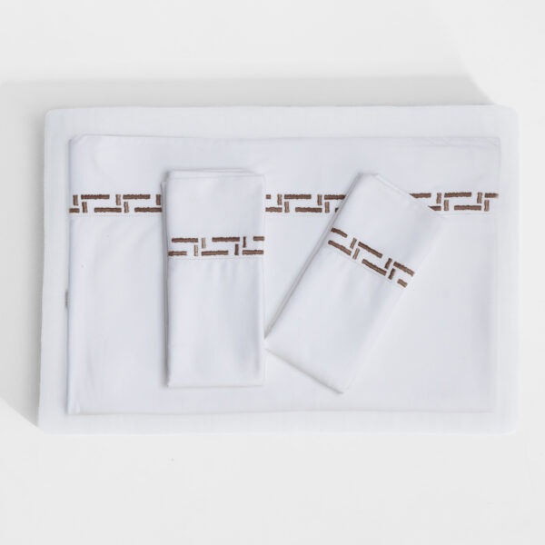 Top down view of white bedding with neatly folded towels and a brown geometric decorative edge strip on the sheets