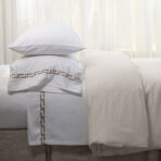 Close up of white pillows and a white duvet on a bed with pale sheer curtains in the background