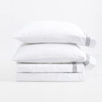 Stack of white pillows with a woven patterned edge on the right set against a white background product photo