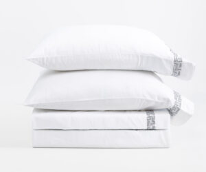 Stack of white pillows with a woven patterned edge on the right set against a white background product photo