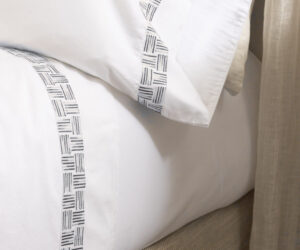 Close up of white fabric with a patterned black and white seam running vertically beige textured upholstery in the background and a light curtain edge