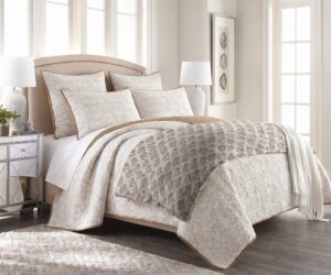 Cream quilted bedding on a tufted headboard bed with decorative pillows in a bright neutral bedroom with large windows