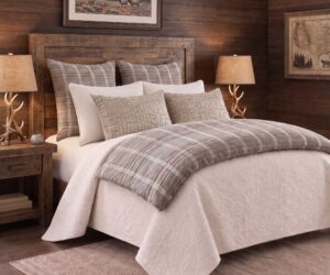 Rustic bedroom with a wooden headboard striped pillows and antler lamps on beside tables against wood paneled walls framed landscape art above the bed