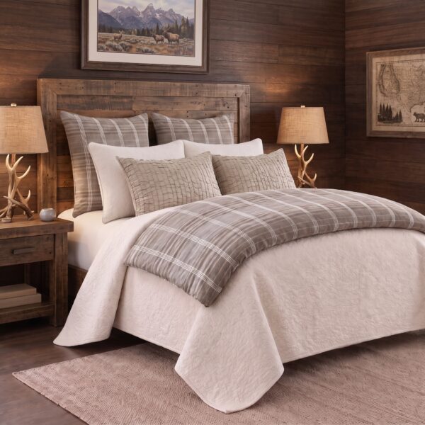 Rustic bedroom with a wooden headboard striped pillows and antler lamps on beside tables against wood paneled walls framed landscape art above the bed
