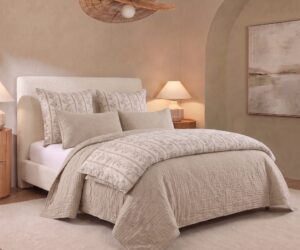 Hotel style bedroom with a cream upholstered bed patterned beige bedding and two bedside lamps