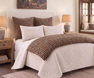 Neutral toned bedroom with a white quilted bedspread brown striped pillows and wooden nightstands framing a cozy headboard