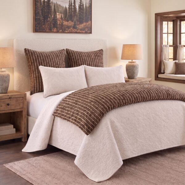 Neutral toned bedroom with a white quilted bedspread brown striped pillows and wooden nightstands framing a cozy headboard