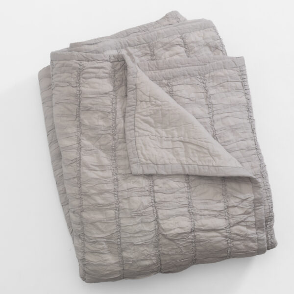 Light gray quilted comforter folded on a white background on a flat surface