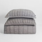 Stack of three pale gray quilted pillows stacked on a white background