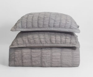 Stack of three pale gray quilted pillows stacked on a white background