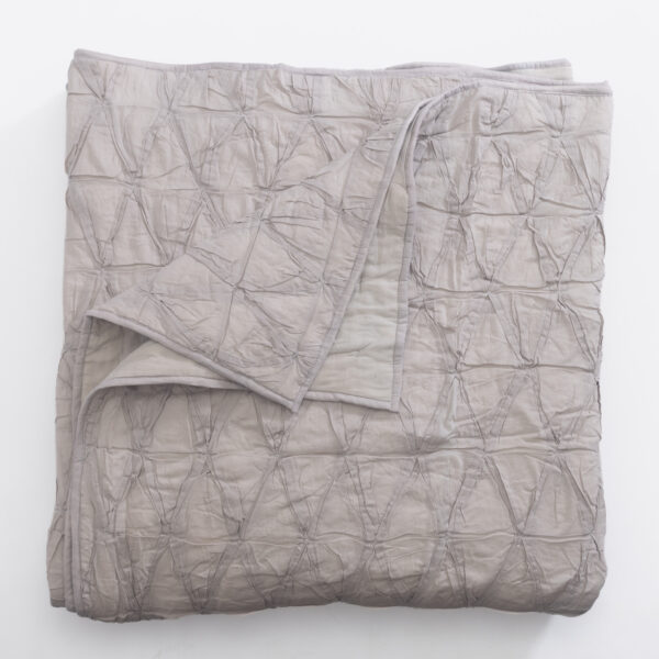 Light gray quilt with a quilted crinkled texture laid flat on a white background