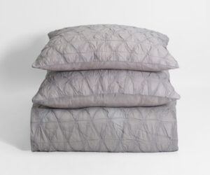 Stack of light gray quilted pillows on a white backdrop centered in the frame