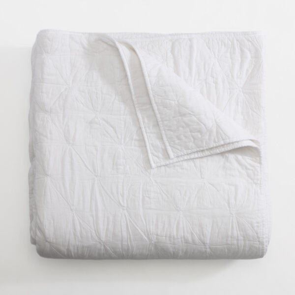 White quilted blanket folded on a light surface showing stitched diamond pattern and soft texture
