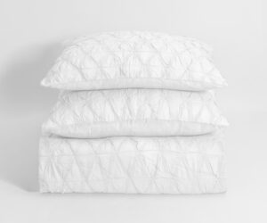 Stack of three white quilted pillows arranged in a vertical stack against a plain light background