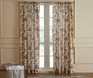 Beige living room with leaf pattern curtains over french doors a gray shag rug a brown floor pillow and a small table draped with a white throw blanket