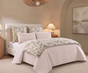 Bedroom with a white upholstered bed floral pattern pillows and a soft beige palette lamps on either side and a woven pendant light overhead