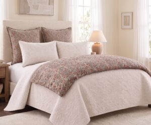 Cream toned bedroom with a tufted headboard beige quilt and floral patterned pillows beside a wooden nightstand and lamp