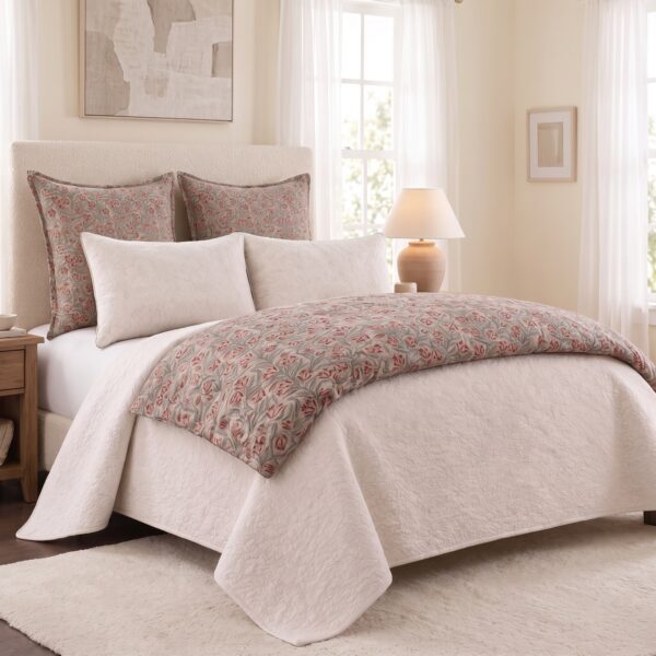 Cream toned bedroom with a tufted headboard beige quilt and floral patterned pillows beside a wooden nightstand and lamp