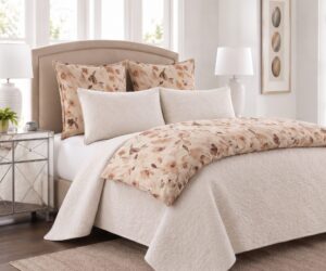 Neutral bedroom with a tufted beige headboard floral patterned pillows and a cream quilt in a bright space with mirrored nightstands and lamps on either side of the bed