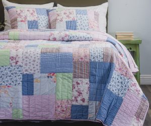 Amity home lattice patchwork quilt set   a cozy bed with a quilt and two pillows featuring various floral striped and gingham patterns in pink blue green and white