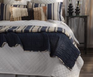 Amity home camden quilt   blue textured quilt draped over a bed revealing a striped beige and navy reverse styled with pillows