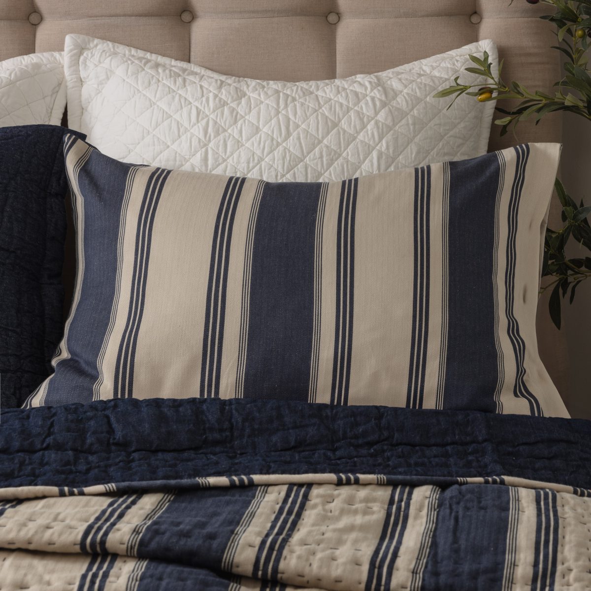 Amity home camden quilt   blue and natural striped quilt with visible hand quilting styled on a bed with a matching pillow