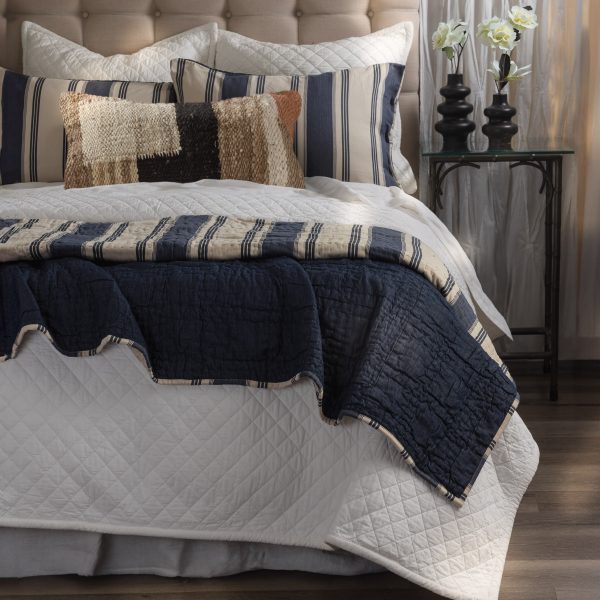 Amity Home Camden Quilt - blue textured quilt draped over a bed, revealing a striped beige and navy reverse, styled with pillows.