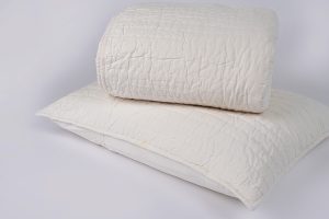 Amity home base camp quilt in ivory folded on a matching pillow sham featuring a crinkled horizontally quilted texture