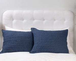 Amity home base camp quilted shams in navy blue featuring a crinkled texture on a white bed