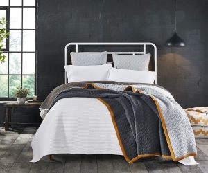 Amity home jade quilt   charcoal grey diamond quilted with mustard trim draped over an ivory bedspread on a modern bed