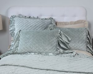 Amity home estrella quilt in sea glass velvet with diamond quilting styled on a bed with matching ruffled pillows