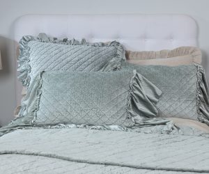 Amity home estrella quilt in sea glass velvet with diamond quilting styled on a bed with matching ruffled pillows