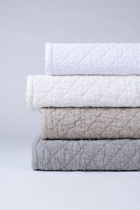 Amity home dale linen quilt in ivory folded and stacked with white beige and grey diamond quilted linen quilts