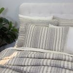 Amity home aiden quilt   grey and cream vertical striped quilt with quilted texture styled on a bed with matching pillows