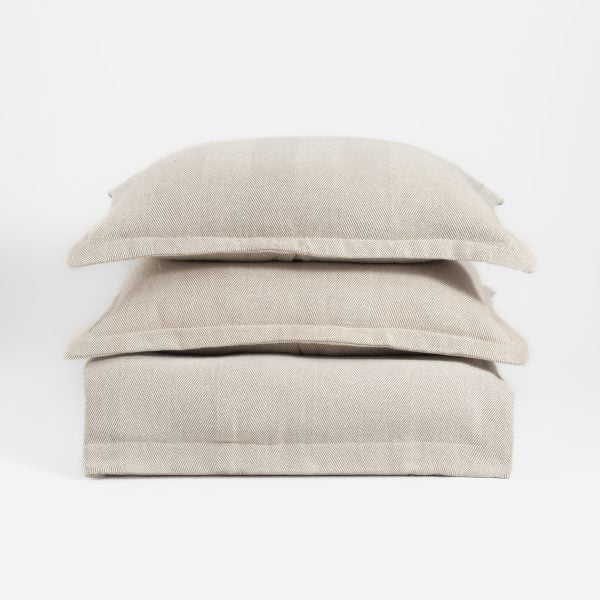 Amity Home Titus Coverlet and two pillows in natural beige, featuring a soft herringbone weave texture, stacked neatly.