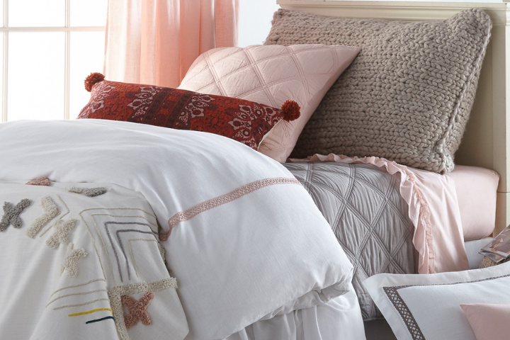 A bed with various textured pillows, soft pink and white bedding, with an embroidered blanket.