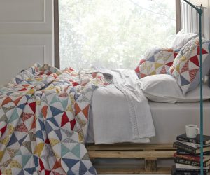 Amity home flying geese quilt   vibrant patchwork quilt with red orange yellow blue and floral triangles draped on a bed
