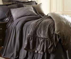Amity home estrella quilt in steel blue featuring a diamond quilted pattern and ruffled edge draped on a luxurious bed