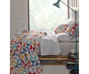 Amity home flying geese quilt   vibrant patchwork quilt with red blue yellow and white triangles on a styled bed