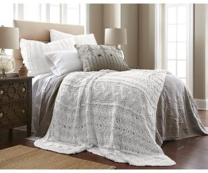 Amity home micah knitted coverlet   white intricate cable knit pattern draped over a bed with layered luxury bedding