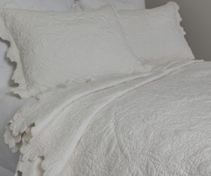 Amity home shantoon quilt in vanilla featuring a subtle quilted floral pattern and scalloped edges styled on a bed with matching pillows