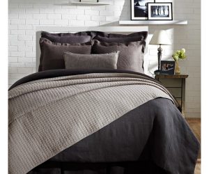 Amity home urban quilt   light grey textured quilt with a subtle grid pattern draped over dark grey bedding on a bed